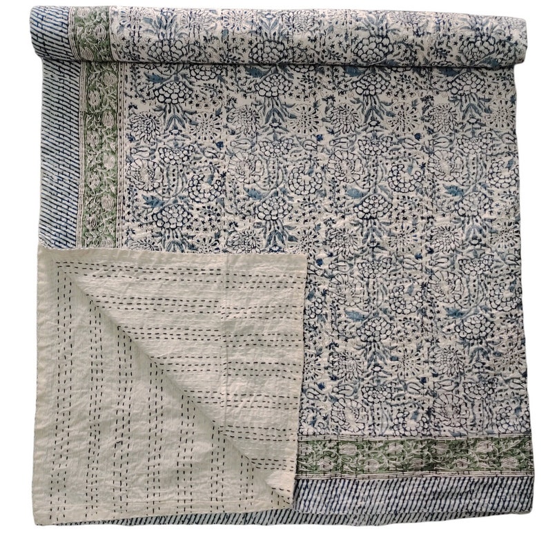May include: A white cotton quilt with a blue floral pattern and green border. The quilt is folded in half and the inside is visible.