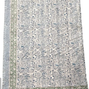 May include: A white cotton quilt with a blue and green floral pattern. The quilt has a border with a green and white striped pattern.