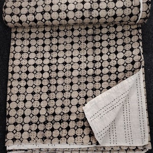 Op de afbeelding: Een zwart-witte kantha-deken met een herhalend patroon van kleine cirkels. De deken is dubbelgevouwen en de onderkant is zichtbaar, waardoor de stiksels zichtbaar zijn.