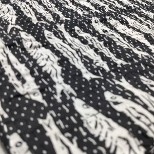 May include: Black and white fabric with a repeating pattern of fish skeletons. The fabric has a textured, slightly wrinkled appearance.