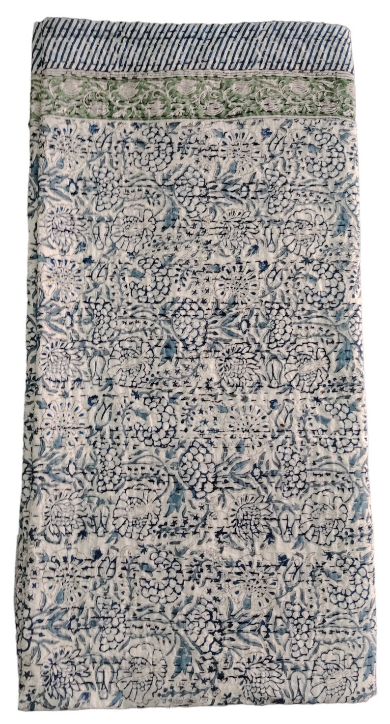 May include: A white cotton quilt with a blue and green floral pattern. The quilt has a border with a striped pattern.