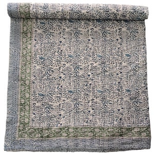May include: A white cotton quilt with a blue and green floral pattern. The quilt has a green border with a white and blue striped pattern.