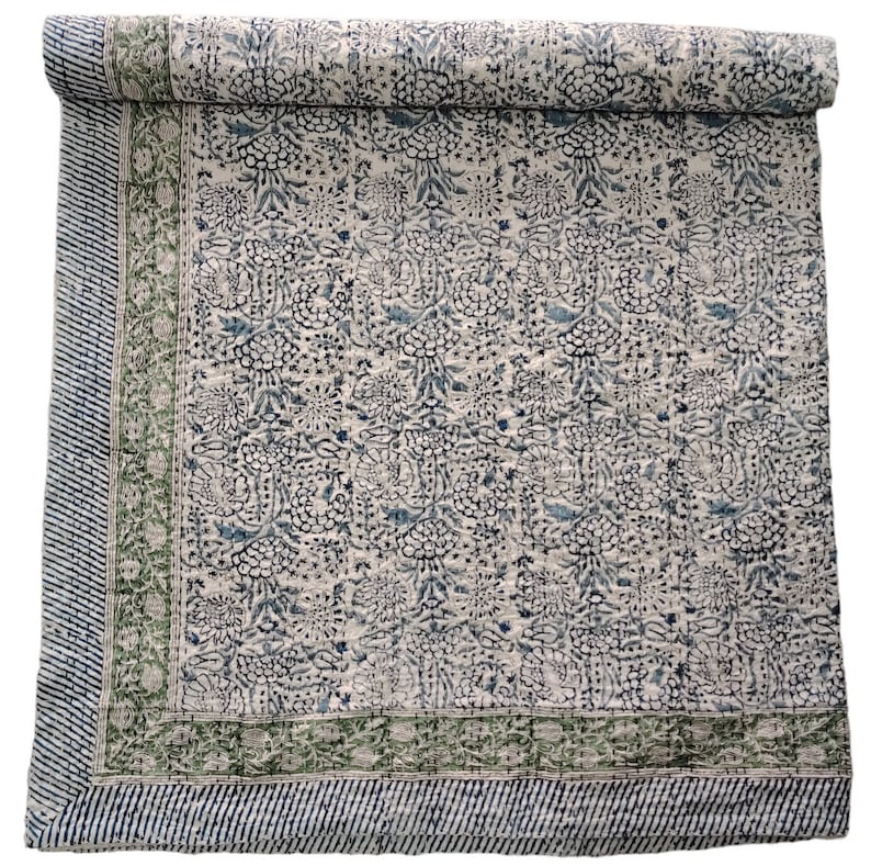 May include: A white cotton quilt with a blue and green floral pattern. The quilt has a green border with a white and blue striped pattern.