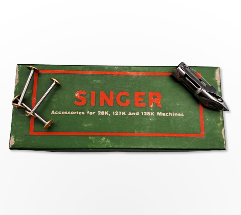 Puede incluir: Una caja verde con la palabra "SINGER" en letras rojas y el texto "Accessories for 28K, 127K and 128K Machines". La caja contiene un accesorio de m&aacute;quina de coser plateado y cuatro carretes plateados con centros dorados.