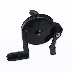 May include: A black manual pencil sharpener with a hand crank. The sharpener has a circular body with a handle and a small gear mechanism. The crank is attached to the side of the sharpener.