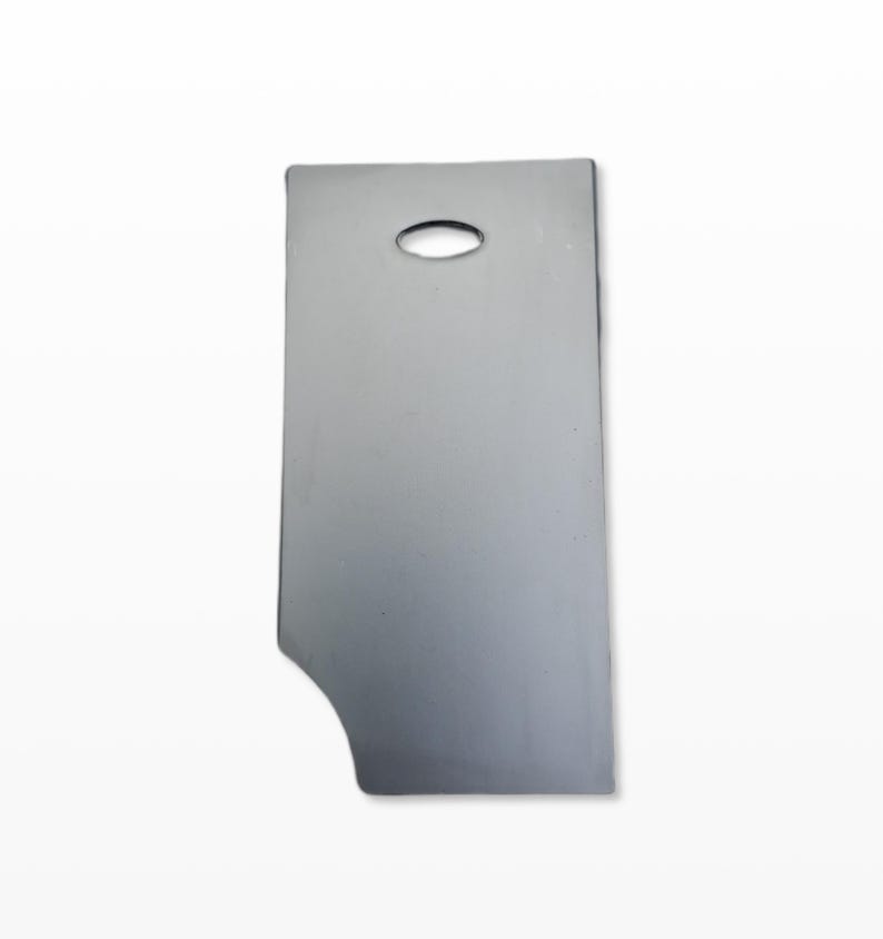 May include: A silver-coloured metal object, rectangular with a curved section on one side and a small oval hole near the top. The object has a smooth, reflective surface, possibly a tool or component.