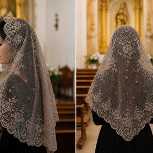 May include: A beige lace mantilla, a traditional head covering, is draped over a person's head and shoulders. The delicate lace features floral patterns and a scalloped edge. The person is wearing a black dress, and the background is a church interior.