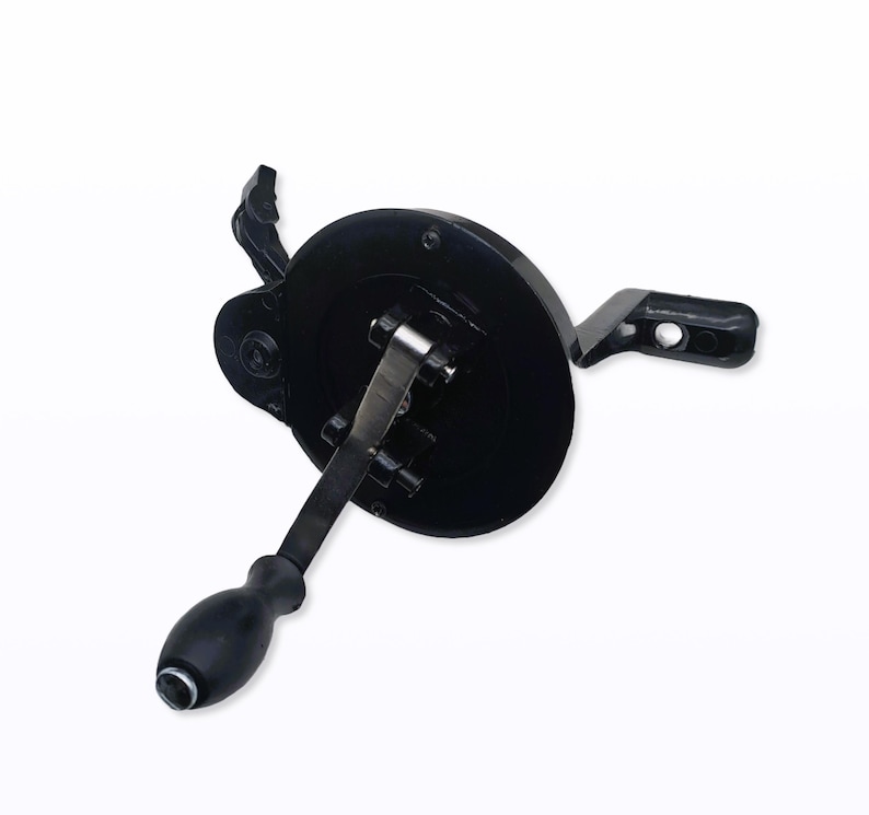 May include: A black hand-cranked mechanism with a circular base, a handle, and a lever. The handle is rounded and black, and the lever is silver. The mechanism appears to be made of metal and plastic.