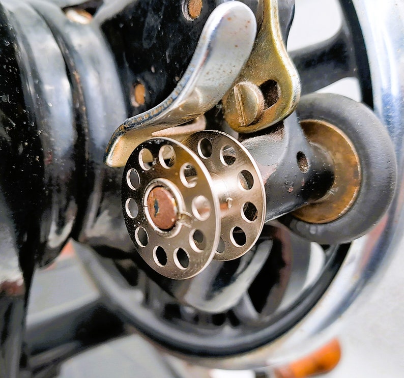 May include: Close-up of a vintage sewing machine with a silver metal spool holder and a black metal base.