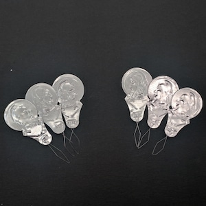 May include: Six silver threader tools with a needle and a small metal loop. Each tool has a different design of a person's face.