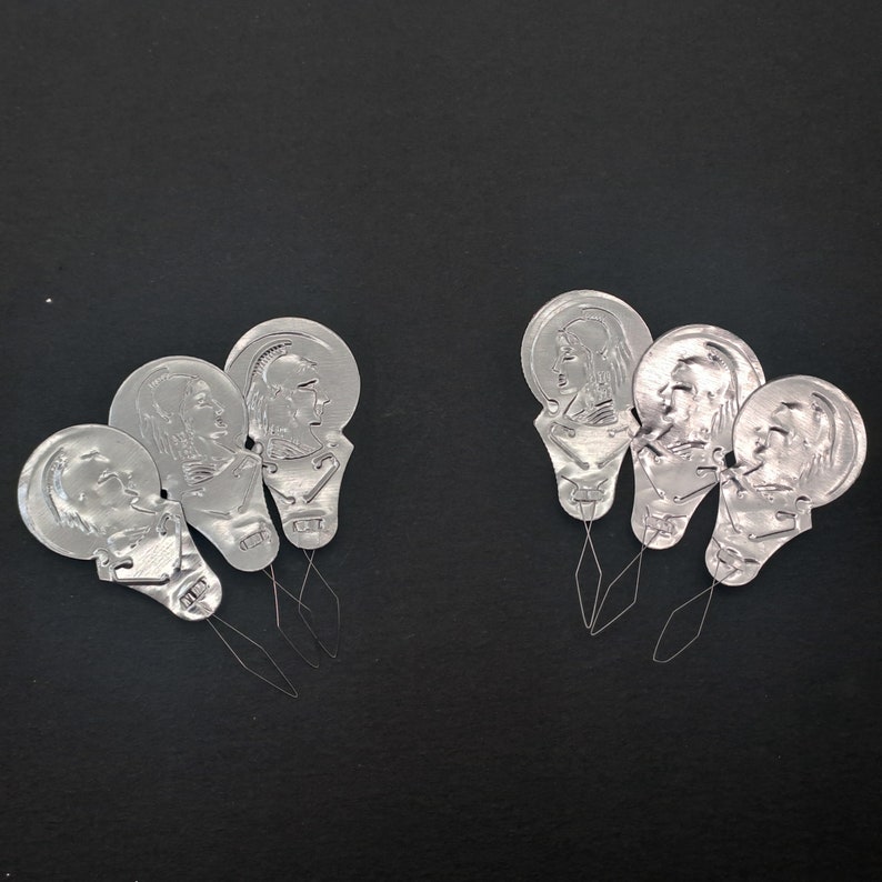 May include: Six silver threader tools with a needle and a small metal loop. Each tool has a different design of a person's face.