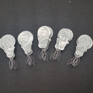 May include: Five silver threader tools with a person's face on each one. The tools are designed to help thread a needle.