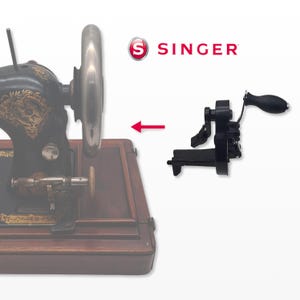 以下が含まれることがあります： 黒と金のデザインのアンティークシンガーミシン。ハンドル付きの黒いアタッチメントがミシンの横に表示されています。シンガーのロゴは右上にあります。