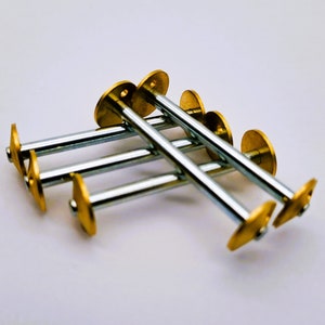 May include: A set of five gold-toned metal push pins with silver metal shafts. The push pins are arranged in a stack, with the heads of the pins facing up.