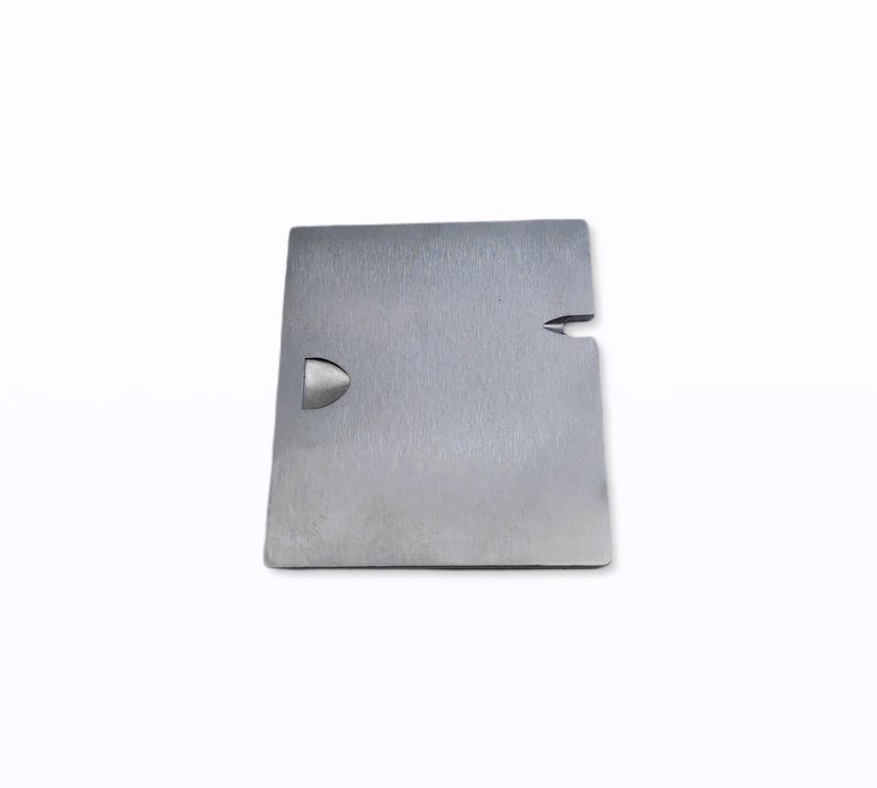 May include: A square, brushed metal object with a rounded cutout on one side and a small notch on the other. The object is silver and appears to be made of a solid, durable material. The background is plain white.