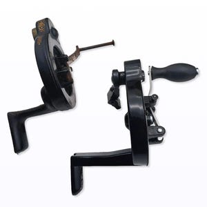 May include: Two antique black metal sewing machine parts. One part has a circular wheel with a handle, and the other has a crank handle. The parts are set against a white background.