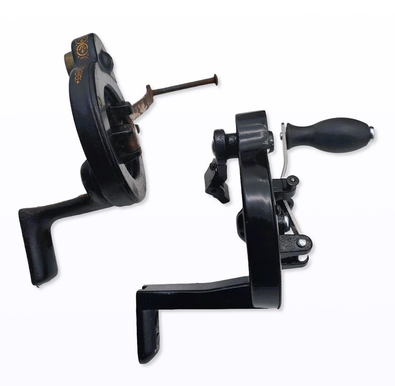 May include: Two antique black metal sewing machine parts. One part has a circular wheel with a handle, and the other has a crank handle. The parts are set against a white background.