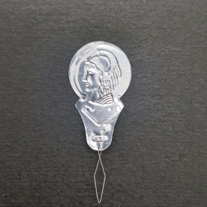 May include: Silver metal needle threader with a design of a woman's head in profile. The threader has a small loop at the end of a thin metal wire.