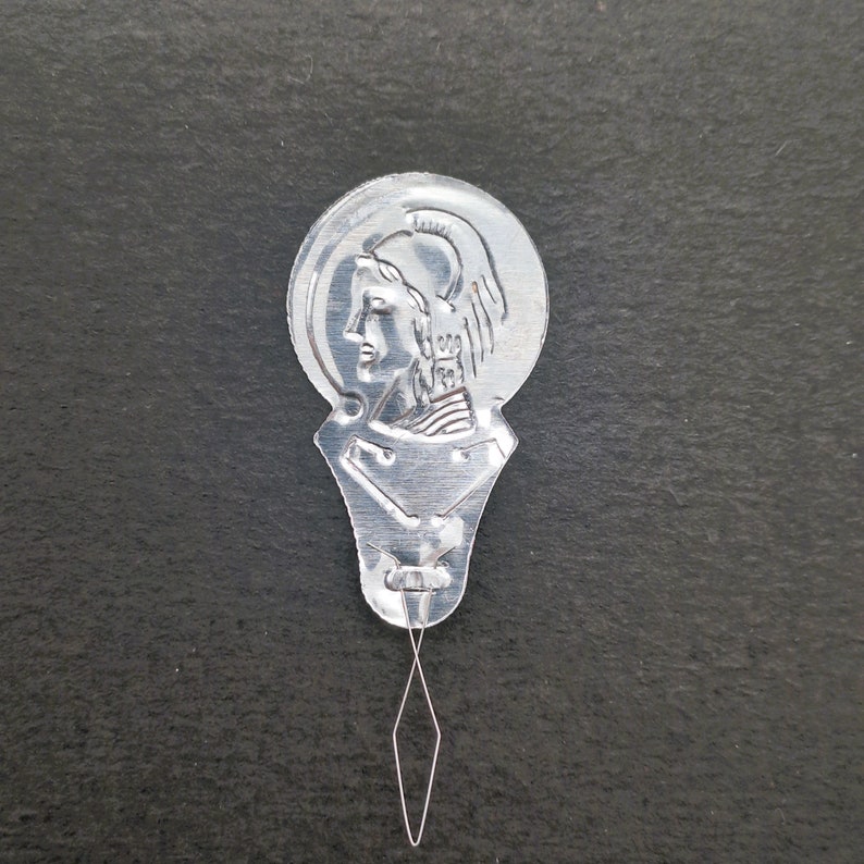 May include: Silver metal needle threader with a design of a woman's head in profile. The threader has a small loop at the end of a thin metal wire.