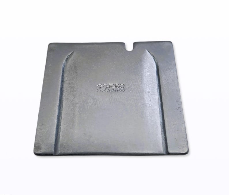 May include: A silver-colored, rectangular metal object with a recessed area and the number "32569" stamped on the surface. The object has a notch on one side and appears to be a mold or a part of a larger mechanism.