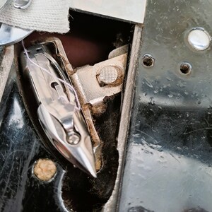 Puede incluir: Primer plano de una aguja de m&aacute;quina de coser y un enhebrador. La aguja es plateada y el enhebrador es un gancho de metal con una peque&ntilde;a perilla redonda texturizada.