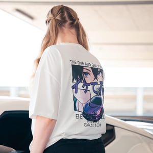 Könnte beinhalten: Weißes T-Shirt mit einem Aufdruck auf der Rückseite mit Augen im Anime-Stil, einem lila Sportwagen und japanischem Text. Der Text "THE ONE AND ONLY" befindet sich über der Grafik. Das T-Shirt hat kurze Ärmel.