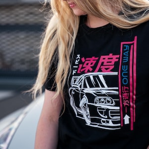 Könnte beinhalten: Schwarzes T-Shirt mit einem weißen Grafikdruck eines Autos und japanischem Text, der "Drift" und "One Way" auf Englisch lautet. Das Auto ist ein weißer Toyota Supra.