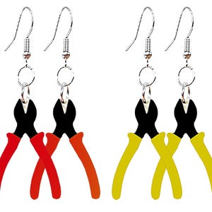 May include: A pair of silver hook earrings featuring a black and red pliers design. The pliers have a black body and red handles. The earrings are a fun and unique accessory.