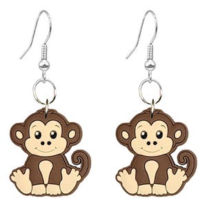 Puede incluir: Un par de pendientes colgantes con un diseño de mono de dibujos animados. Los pendientes tienen un gancho plateado y un accesorio circular. El mono es marrón con la cara, las manos y los pies de color beige. El mono está sentado con las manos en las rodillas.