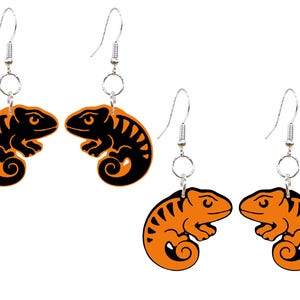 May include: Orange and black chameleon earrings. The earrings feature a stylized chameleon design with a black outline and orange fill. The earrings have silver-colored hooks.