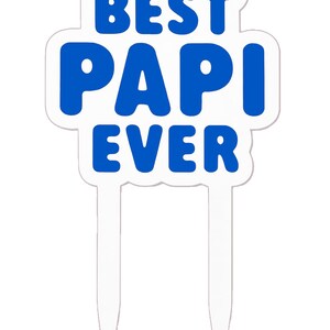 Puede incluir: Un adorno para pastel blanco con las palabras "BEST PAPI EVER" en azul. El adorno tiene forma rectangular redondeada y dos púas de plástico transparente para insertar en un pastel.