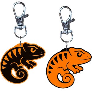 May include: Two chameleon keychains. One is black with orange stripes, the other is orange with black stripes. Each keychain has a silver-colored clasp for attaching to keys or bags.