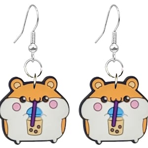 May include: A pair of novelty earrings featuring a cartoon hamster design. The earrings have a silver hook and a charm depicting a hamster drinking bubble tea. The hamster is orange, white, and black.