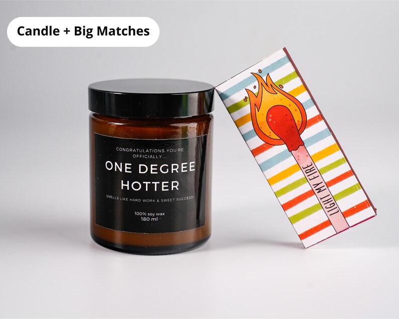 May include: A brown glass jar candle with a black lid and a label that reads "ONE DEGREE HOTTER." A decorative matchbox with a colorful striped design and a lit match illustration is leaning against the candle. The text "LIGHT MY FIRE" is printed on the matchbox.