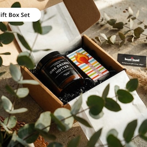 May include: A gift box set containing a jar of "ONE DEGREE HOTTER" candle, a matchbox with a colorful striped design, and a business card. The box is brown and lined with white paper and black filler.