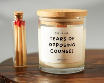 Può includere: Un barattolo di candela in vetro trasparente con coperchio in legno e un'etichetta che recita "Smells Like Tears of Opposing Counsel". Accanto alla candela c'è una piccola bottiglia di vetro di fiammiferi. La candela è fatta di cera di soia al 100%.