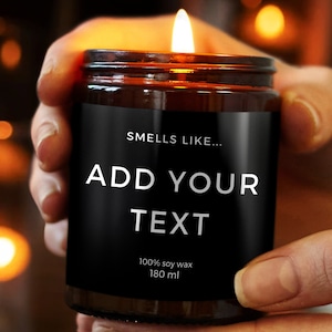 Könnte beinhalten: Eine braune Glaskerze mit einem schwarzen Etikett, auf dem "Smells Like... Add Your Text 100% soy wax 180 ml" steht. Die Kerze ist angezündet und die Flamme ist sichtbar.