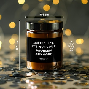 May include: A brown glass candle jar with a black label that reads "Smells Like It's Not Your Problem Anymore." The candle is 8.0 cm tall and 6.5 cm wide, with a burn time of 40 hours. It is made of 100% soy wax.