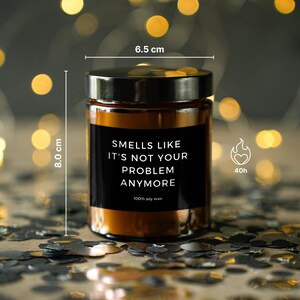May include: A brown glass candle jar with a black label that reads "Smells Like It's Not Your Problem Anymore." The candle is 8.0 cm tall and 6.5 cm wide, with a burn time of 40 hours. Made with 100% soy wax.