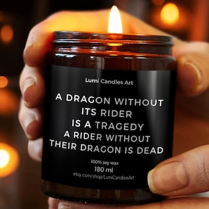 Op de afbeelding: Een brandende kaars in een bruine glazen pot. Het zwarte etiket leest: "A DRAGON WITHOUT ITS RIDER IS A TRAGEDY A RIDER WITHOUT THEIR DRAGON IS DEAD." De kaars bevat 180 ml 100% sojawas.