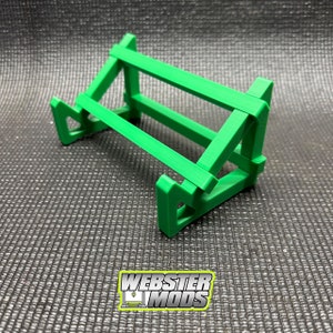 May include: A green plastic phone stand with a simple design. The stand is angled to hold a phone upright.