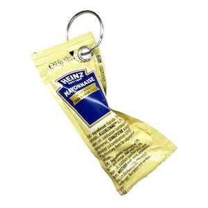 Może przedstawiać: Pojedyncza saszetka majonezu Heinz przymocowana do srebrnego breloka. Saszetka jest żółta z niebieskim i białym tekstem, w tym logo Heinz i słowami "MAYONNAISE" i "MADE WITH FREE RANGE EGGS".