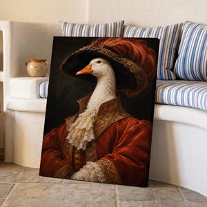 Könnte beinhalten: Ein gerahmtes Porträt einer weißen Gans, die einen dunklen Hut mit breiter Krempe und einer großen roten Feder, einen roten Samtmantel mit goldener Stickerei und ein weißes Spitzenjabot am Hals trägt. Das Bild hat einen dunklen Hintergrund.