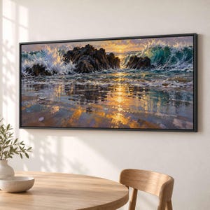 Könnte beinhalten: Ein rechteckiger gerahmter Wandkunstdruck, der eine Küstenszene mit dunklen, zerklüfteten Felsen, brechenden türkisfarbenen Meereswellen und einem goldenen Sonnenuntergang zeigt, der sich auf dem nassen Sand spiegelt. Schwarzer Rahmen.