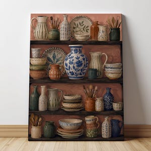 May include: A rectangular canvas print featuring a three-shelf display of assorted ceramic pottery, including pitchers, bowls, plates, and vases in various colors like blue, white, green, and terracotta, arranged against a warm, muted red background.