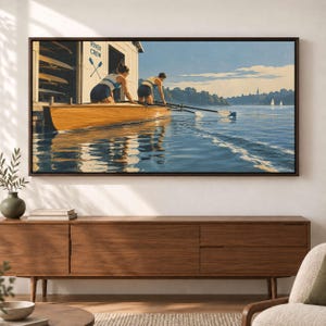 Könnte beinhalten: Ein gerahmter Kunstdruck zeigt zwei Ruderer in einem Holzboot auf einem ruhigen Fluss. Das Bootshaus im Hintergrund trägt die Aufschrift RIVER CREW mit gekreuzten Rudern. Die Szene zeigt blaues Wasser, einen klaren Himmel und Segelboote.