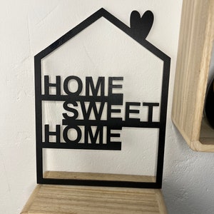 May include: Black metal home decor sign with the words "Home Sweet Home" in a house shape with a heart on top.