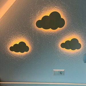 May include: Three black cloud-shaped night lights with a warm yellow glow on a light blue wall. A white electrical outlet is visible below the lights.