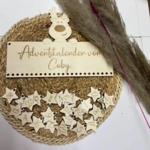 May include: A round Advent calendar with a woven jute base. A wooden sign with the text "Adventskalender von Coby" is at the top, and star-shaped tags numbered 1-24 are below. A wooden reindeer decorates the top.