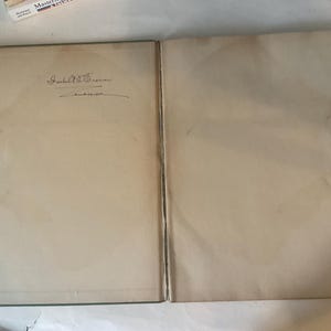 Op de afbeelding: Open boek met verouderde, cr&egrave;mekleurige pagina's. De linkerpagina heeft een handgeschreven handtekening boven een datum. De randen van het boek zijn donkergroen. De pagina's vertonen tekenen van ouderdom en gebruik.